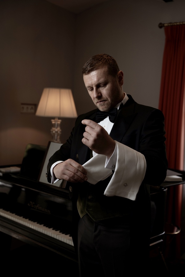 Der Butler richtet am Klavier seine Manschetten